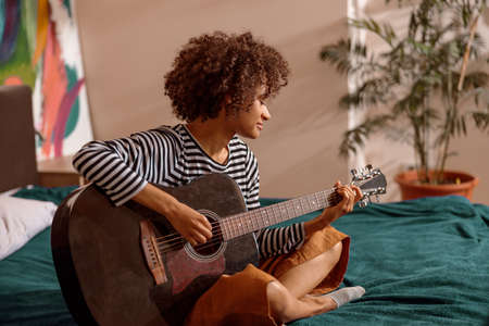 Multiracial young woman playing guitar at homeの写真素材