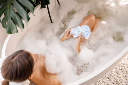 High angle view of relaxed woman lying down in the tub with foam, spending time at luxury spa resortの写真素材