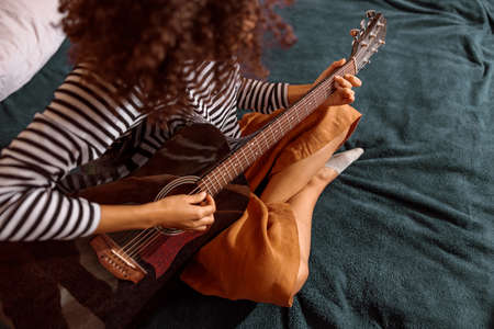Multiracial young woman playing guitar at homeの写真素材
