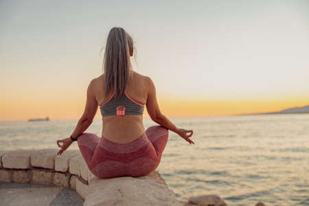 Woman in sportswear sitting in lotus position on the edge of seafrontの写真素材