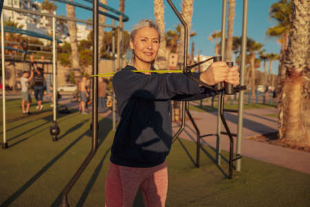 Focused sortswoman in black hoodie exercising outside with rubber bandsの写真素材