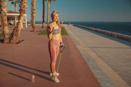 Full-length photo of woman exercising on embankment with fitness rubber bands