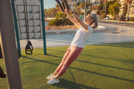 Full-length photo of mature lady in sports clothing exercising at outdoor sports ground