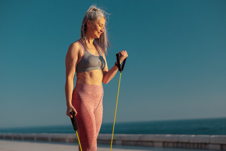 Strong woman in sportswear exercising on sports site, using fitness resistance bandsの写真素材