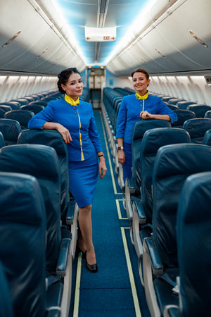 Female flight attendants standing in aircraft passenger cabinの写真素材