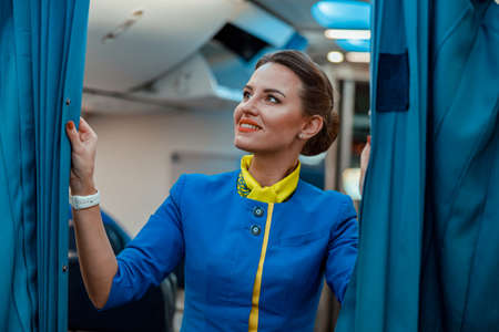 Cheerful woman stewardess holding curtains in airplane