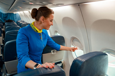 Smiling woman stewardess closing window in airplane