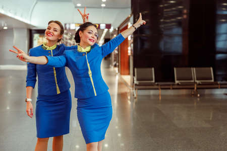 Cheerful women stewardesses showing victory gesture at airportの写真素材