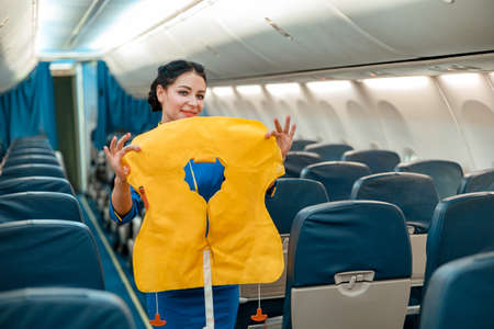 Female flight attendant with life vest standing in airplaneの写真素材