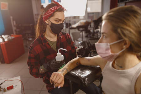 Young tattoo artist in protective mask sitting next to clientの写真素材