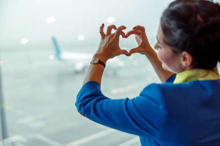 Female flight attendant doing heart symbol at airportの写真素材