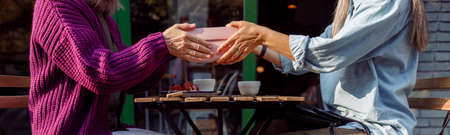 Senior women friends hold gift box above table on outdoors cafe terraceの写真素材