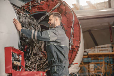 Joyful male mechanic repairing airplane in hangar