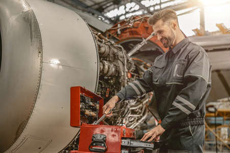 Joyful male mechanic using tool box in hangar