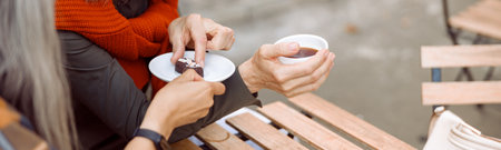 Happy mature woman takes candy from friend at wooden table in street cafe