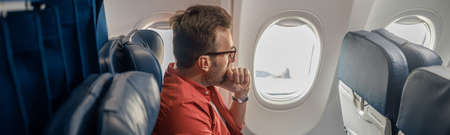 Pensive caucasian man in casual wear resting on the plane, sitting and looking out the windowの写真素材