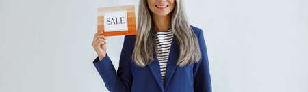 Pretty Asian lady with grey hair holds card with word Sale on light backgroundの写真素材