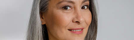 Attractive grey haired mature lady in stylish shirt smiles to camera in studio