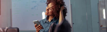 Smiling young lady using mobile phone in the office