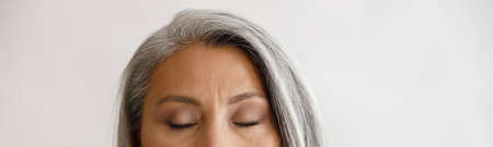 Tranquil grey haired lady with closed eyes and elegant makeup poses on light backgroundの写真素材