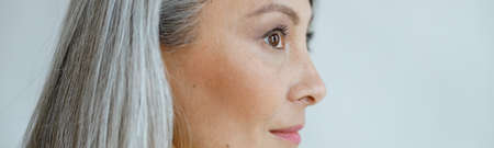 Middle aged Asian woman with beautiful straight hoary hair on light grey backgroundの写真素材