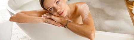 Attractive young woman feeling tired, leaning on bathtub side, bathing while relaxing at spa resortの写真素材