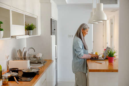 Woman using laptop in kitchen in modern apartmentの写真素材
