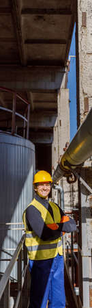 Joyful male engineer standing near metal pipe at factoryの写真素材