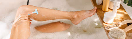Cropped shot of young woman shaving her legs with disposable shaving razor while bathing. Body care...