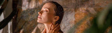 Portrait of young woman standing with eyes closed and washing her body while taking showerの写真素材