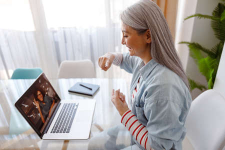 Joyful woman using notebook for online communication with friend
