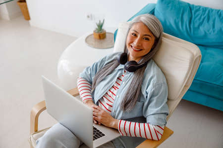 Joyful woman sitting in chair and using notebook at homeの写真素材