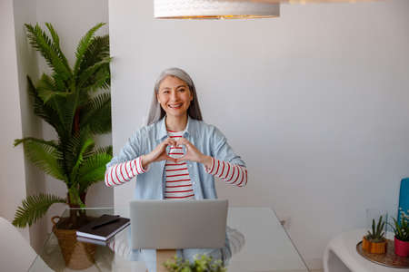 Woman sitting at the table with laptop and doing heart gesture
