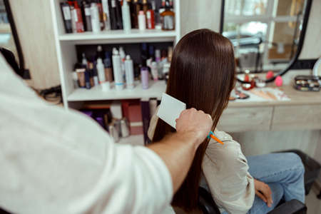 Hairstylist brushing long and shiny brown hair of young woman at beauty salonの写真素材