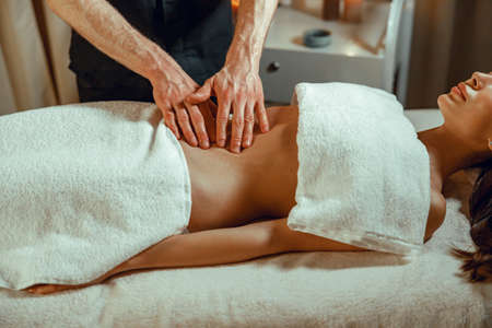 Male manual worker doing stomach massage with fingers to woman in spa salonの写真素材