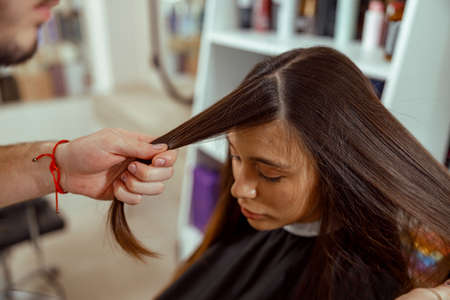 Young female customer sits in a chair covered with a cape while a hair master cuts fringeの写真素材