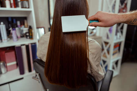 Closeup of hairstylist brushing long and sleek brown hair of female client at beauty salonの写真素材