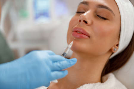 Attractive young woman getting rejuvenating injections in lips at beauty salon