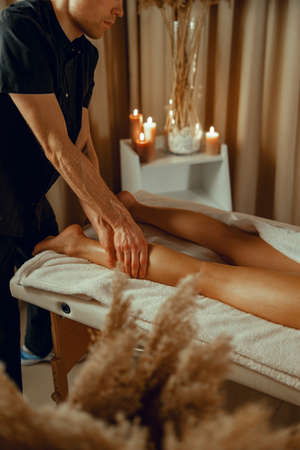 Concentrated male therapist doing professional leg massage for female client at spa centerの写真素材