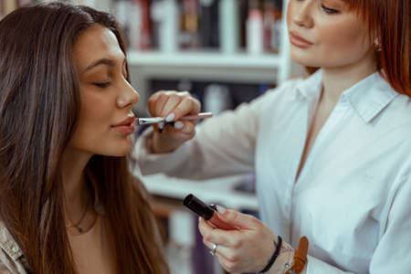 Professional makeup artist applying lipgloss to customer lips at beauty salonの写真素材