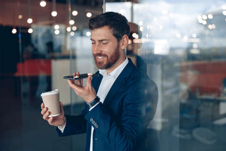 Handsome businessman is using smartphone to record a voice message to business partner