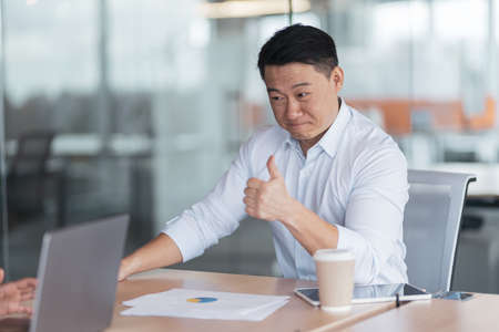Smiling Asian businessman in meeting with colleagues in modern officeの写真素材