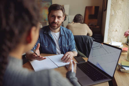 Handsome man at business meeting with female coworker. Male taking notes in notebook.