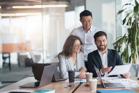 Smiling businessmen drink coffee and discussing documents with graphs and charts