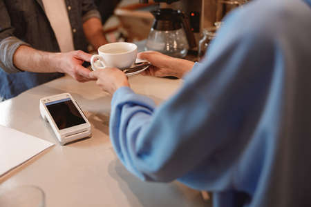Hands of female barista serving coffee at bar and giving cup to male customer. Cafeteria worker.の写真素材