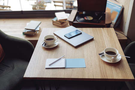 Wooden table with two cups of coffee and business stuff. Cozy place for meeting in cafeteria.