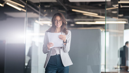 Young smiling businesswoman with documents standing at office and look at cameraの写真素材