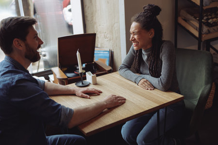 Cheerful mixed-races couple laughing and chatting at table in cafe. Happy man and woman at meeting.の写真素材