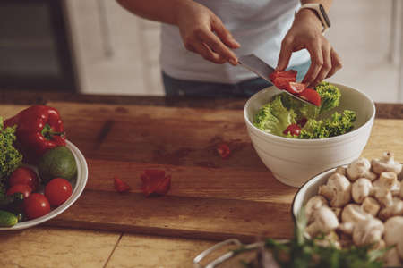 Womens hands with a knife cut vegetables for salad from tomatoes, greens and sweet peppersの写真素材