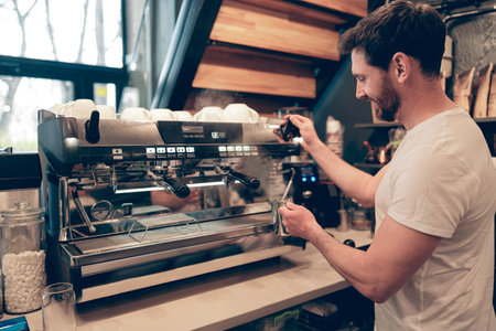 Caucasian smiled male barista making coffee at professional machine in cafeteria. Cafe job.の写真素材
